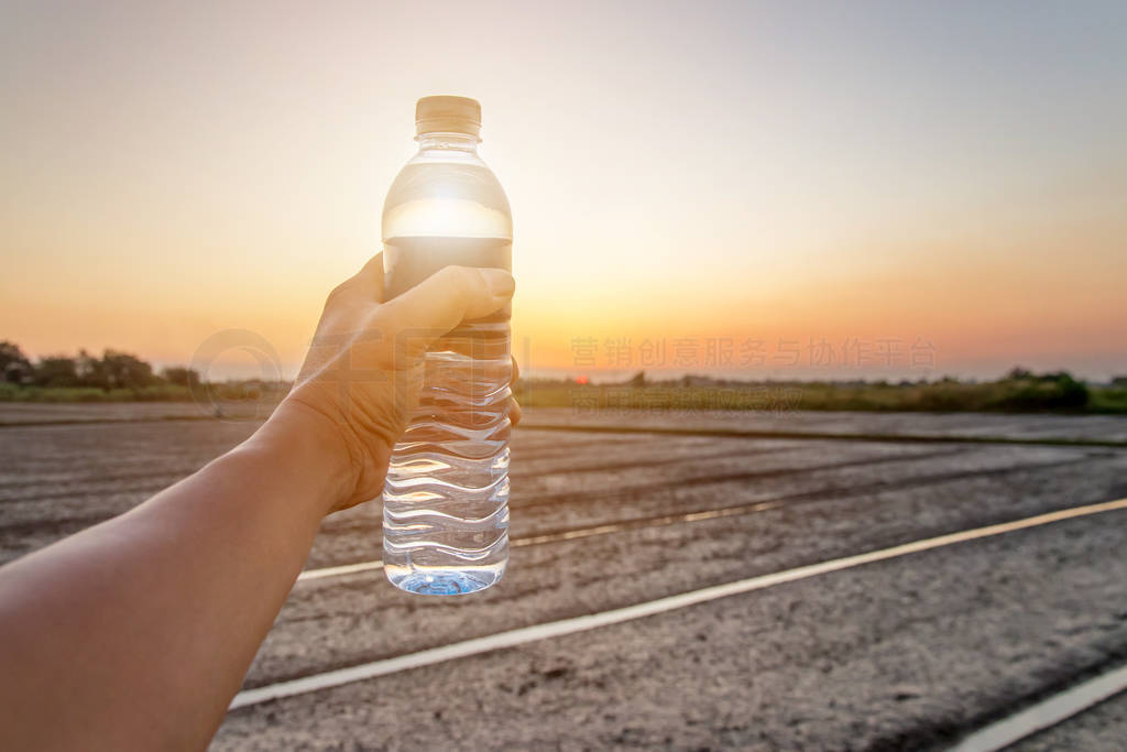 Hand holding bottle water on sunset sky,Summer holiday vacation