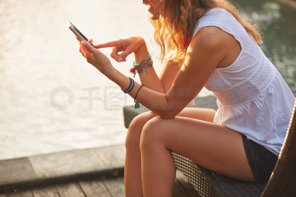 Girl using cellphone while lying on a swimming pool deck lounge