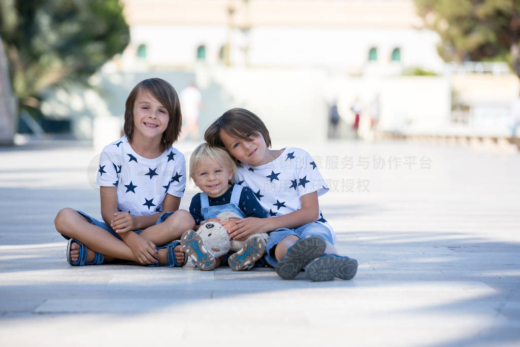 Three cute children, boy brothers, sitting on the ground in the