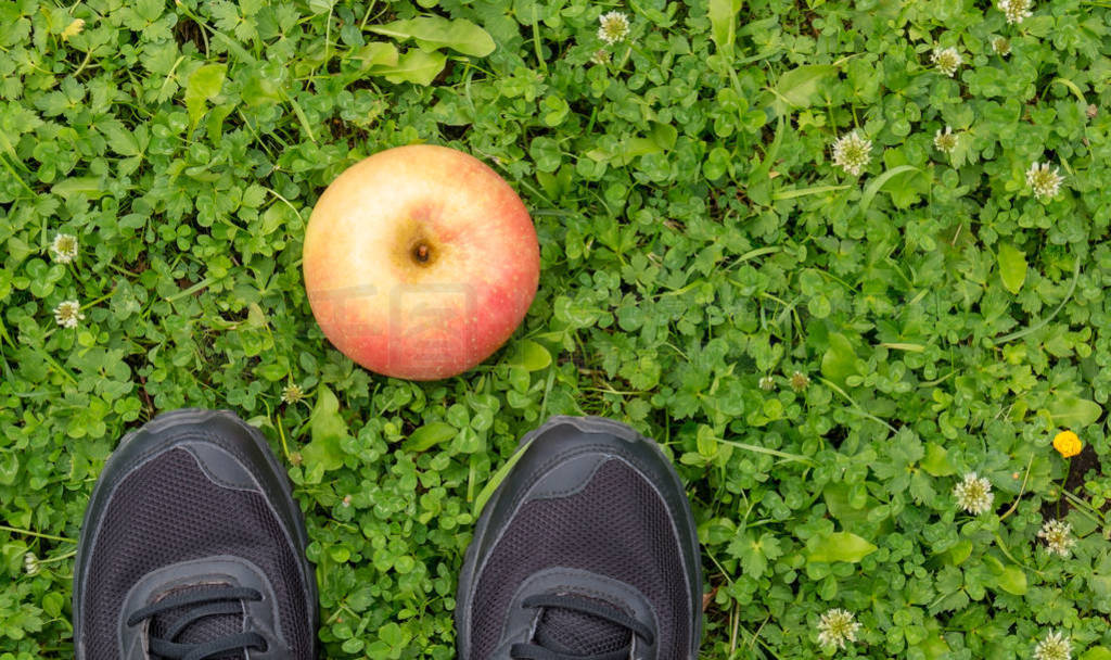 Black sneakers and apple on fresh green grass.