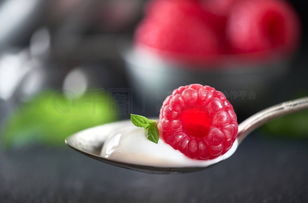 Close-up on a spoon of yougurt with juisy raspberry on top with