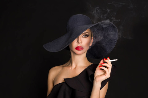 优雅的女人,黑党徽与香烟在手拿着帽子在黑色背景上