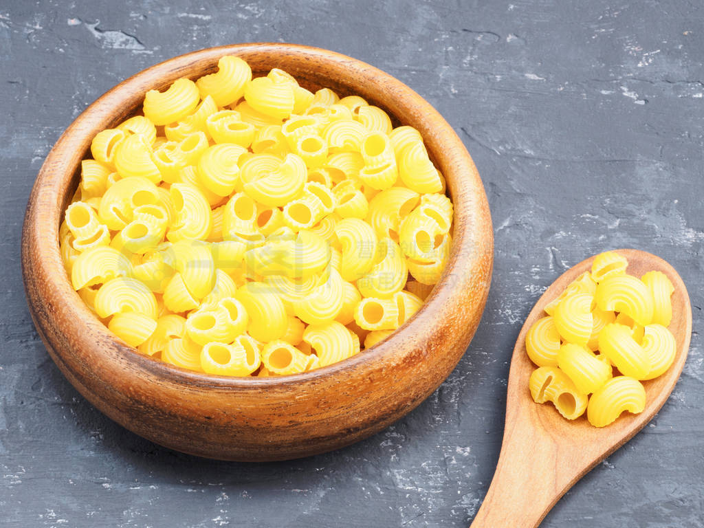 Pasta helices type in wooden bowl and spoon on a black concrete