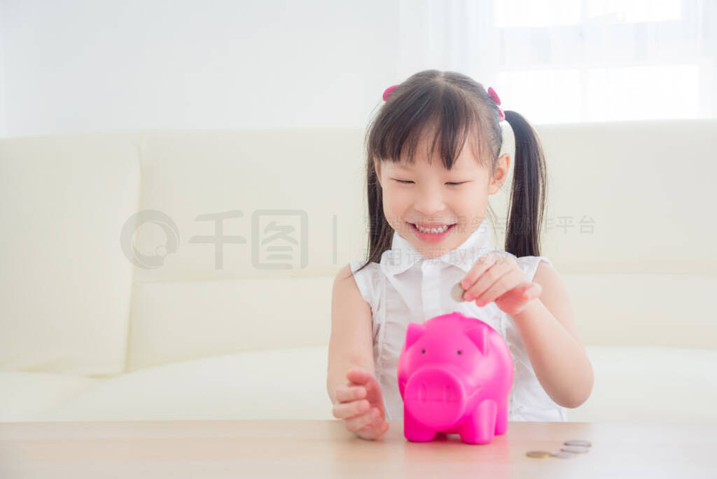 Little asian girl inserting coin into pink piggy bank