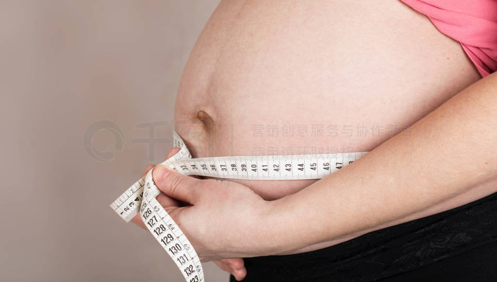 Young pregnant woman measures her belly with measurement band.