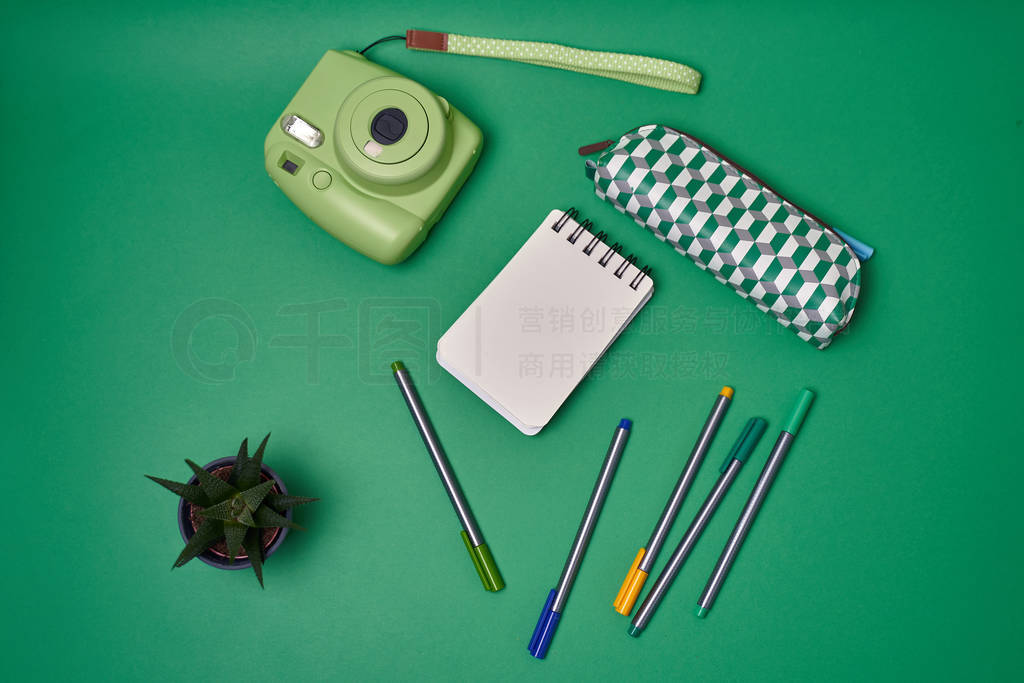 Notebook, pens and instax camera on green background