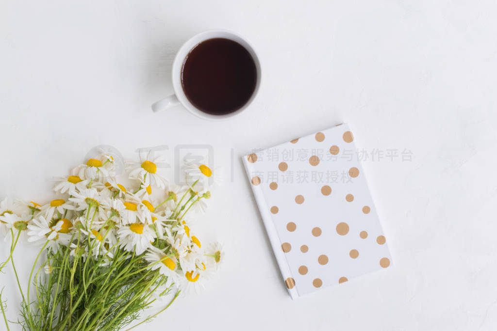 Flat lay desk with white daisies, notebook and cup with tea