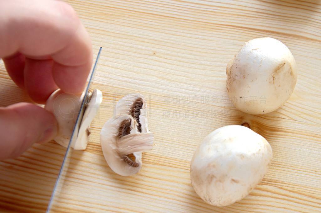The hand of a cook holds a knife and cuts mushrooms on a wooden