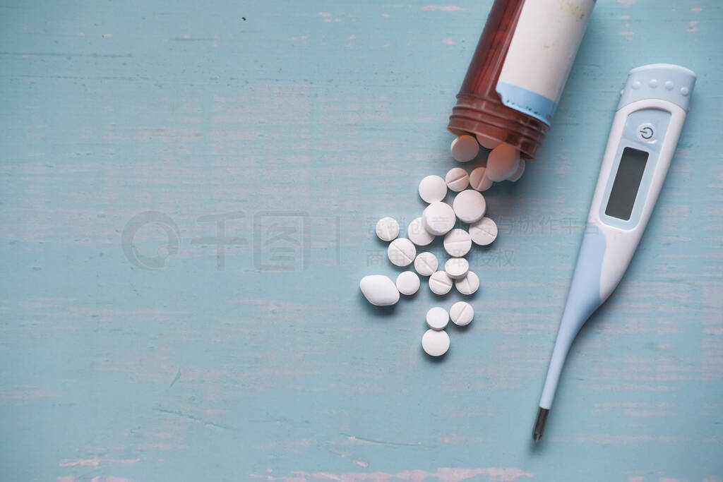 white pills spilling from container and thermometer on table