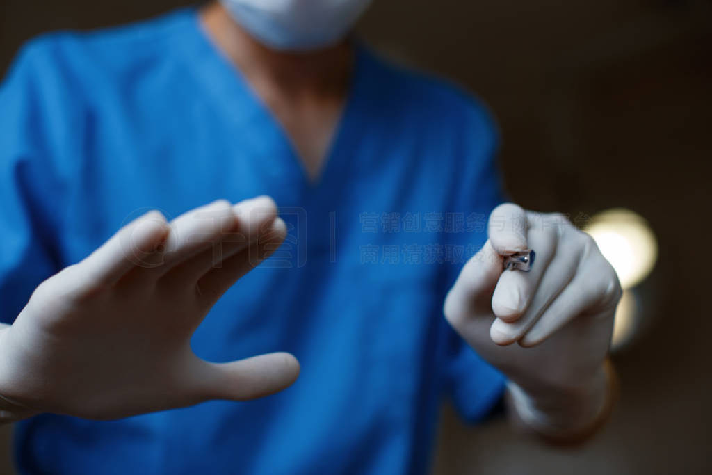 s hands in sterile latex gloves hold a surgical metal scalpel ag