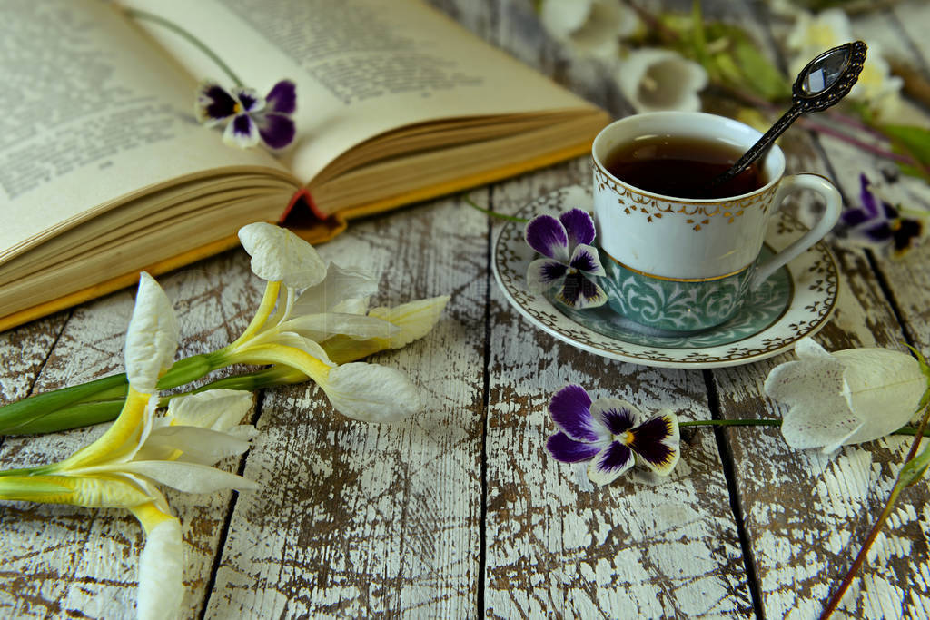 Open book of poetry, old cup of tea and flowers on table.