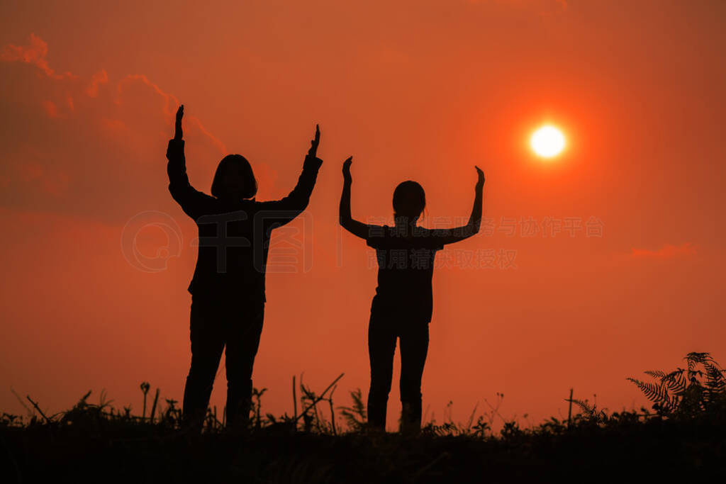 Silhouette of two teen girls praying to god with the bible.