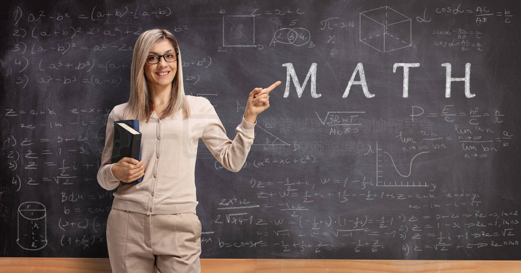 Smiling math teacher holding books and pointing to a blackboard