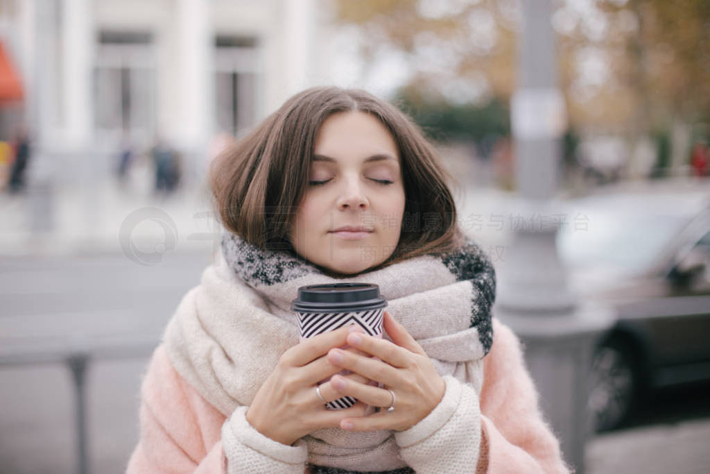 Woman in pink trendy coat drinking coffee on street.