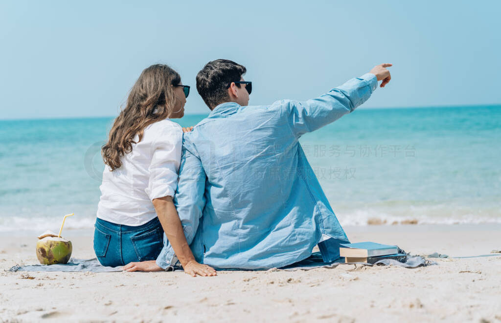 Back view of a couple sitting together on beach towel along the