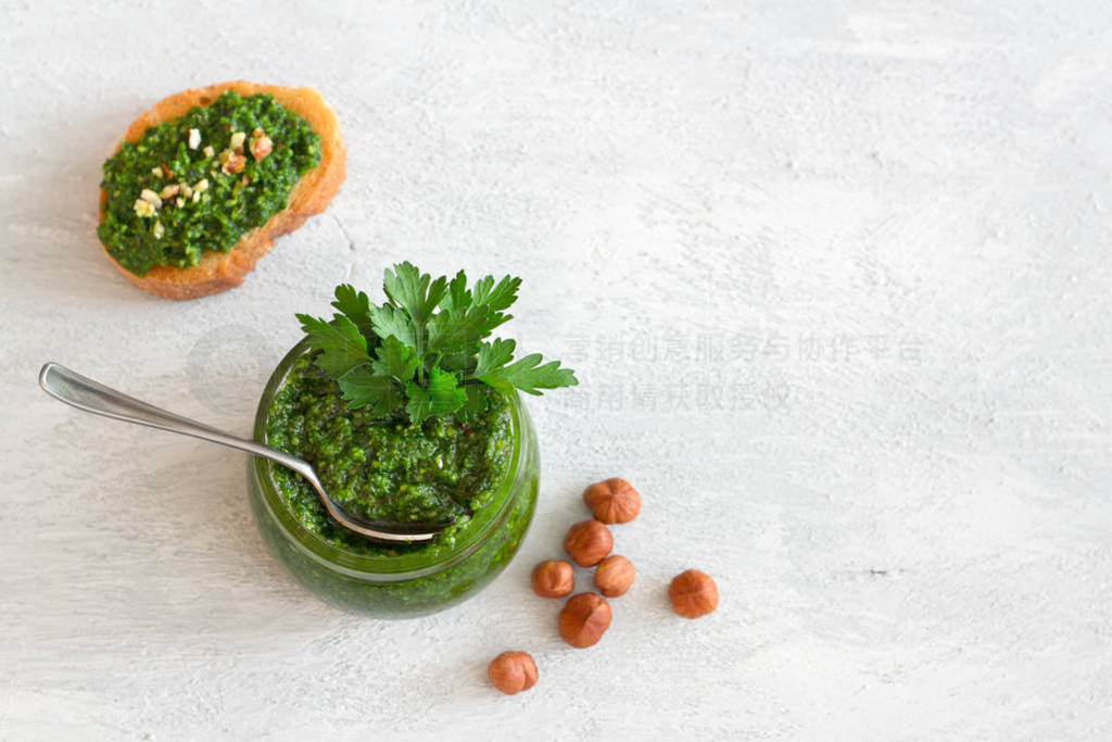 Fresh homemade parsley pesto with hazelnuts in glass jar and bre