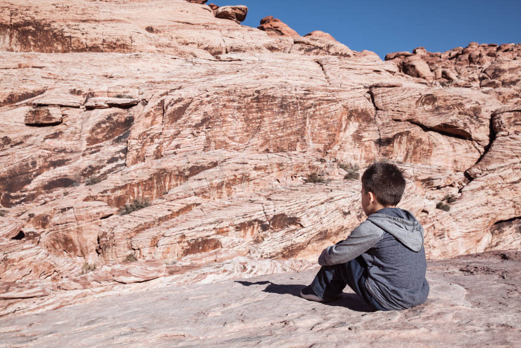 Little boy sitting on rocks and enjoying view of mountains on a