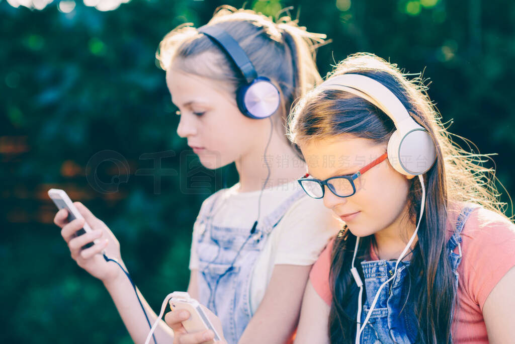 Two teenagers listening to music from smartphones
