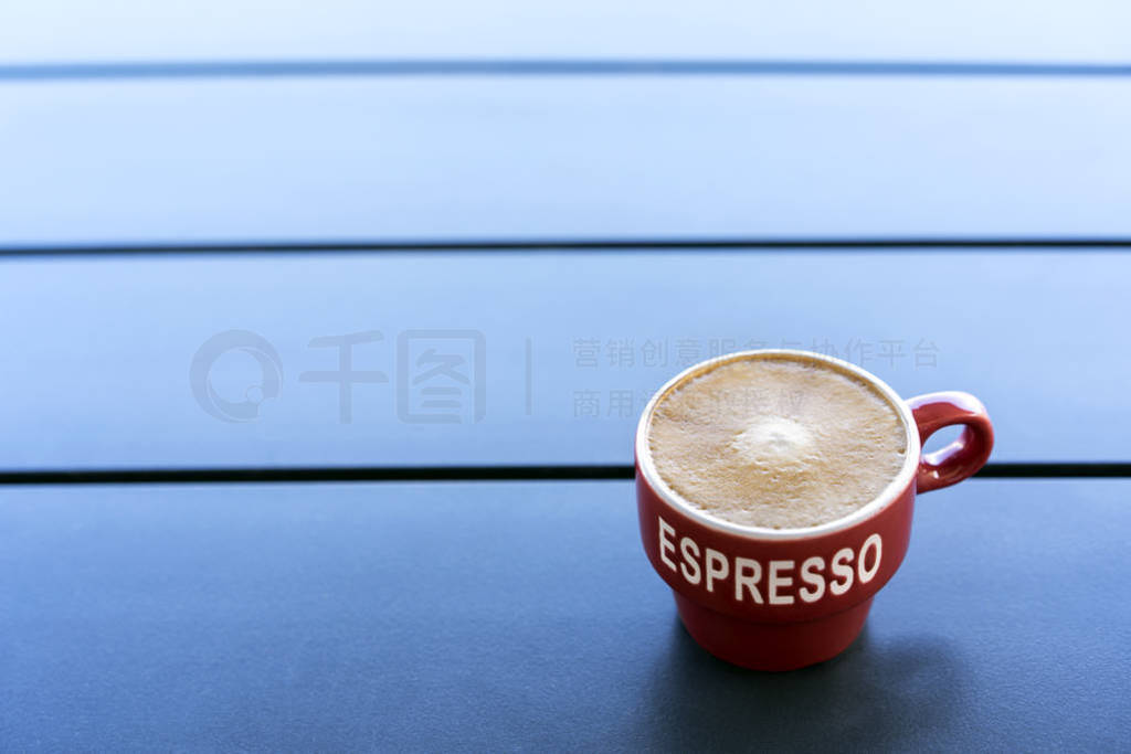 Small red cup of espresso with foam on the table.