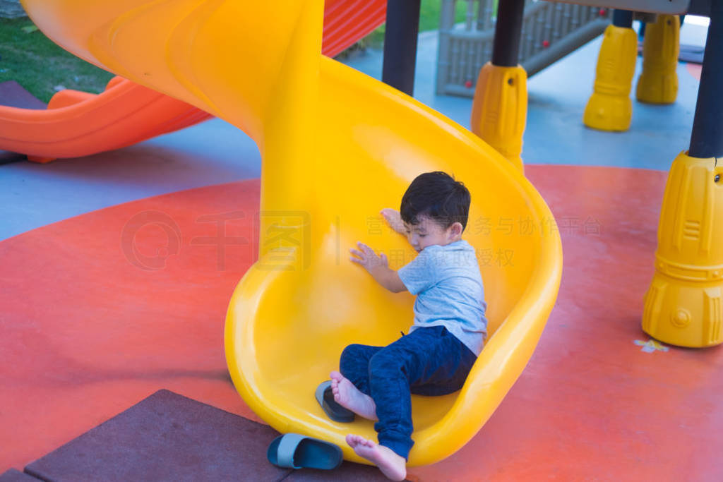 Asian kid playing slide at the playground under the sunlight in
