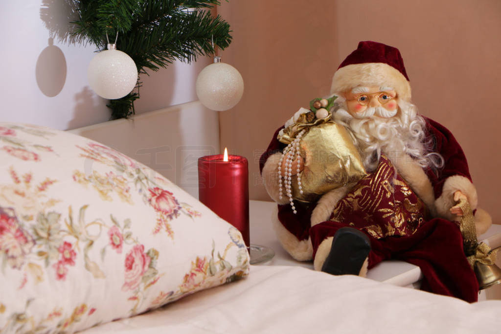 At Christmas, Santa Claus sits with a gift near the bed next to