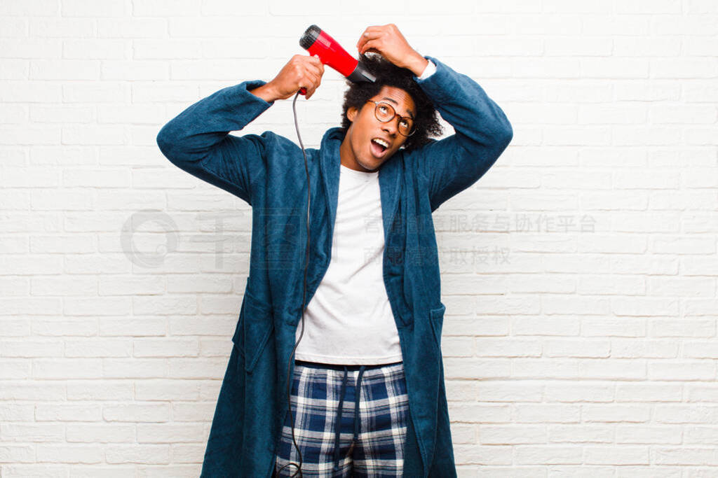 young black man wearing pajamas with a hair dryer against brick