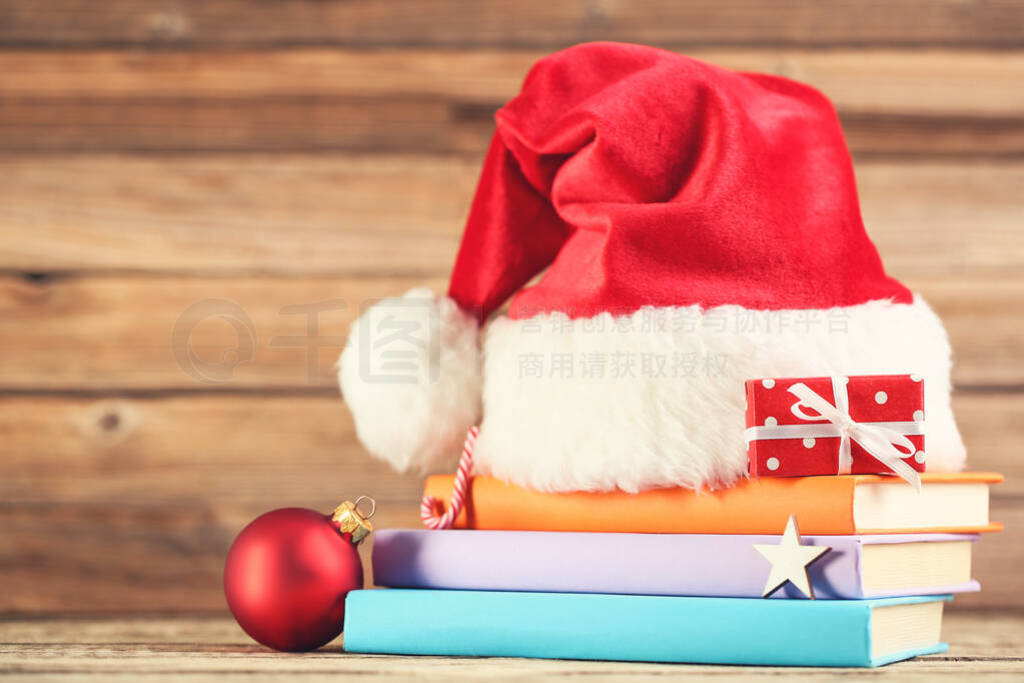 Red santa hat with stack of books, gift box and bauble on brown