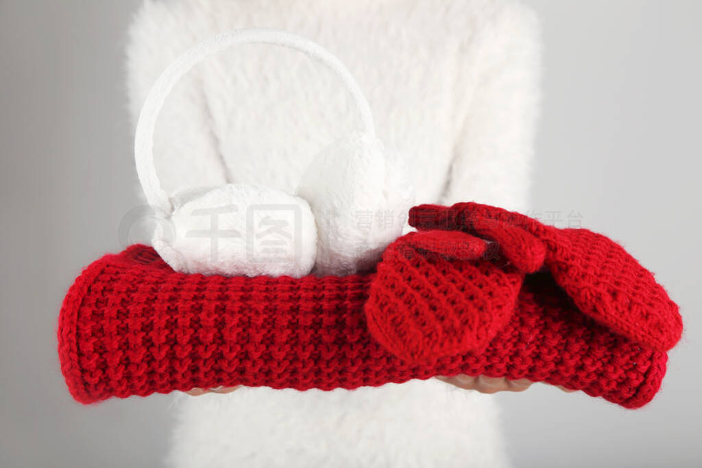 Female hands holding knitted scarf, pair of gloves and earmuffs