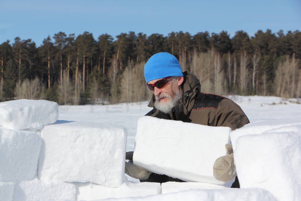 Man in a blue hat building an igloo from snow snow blocks