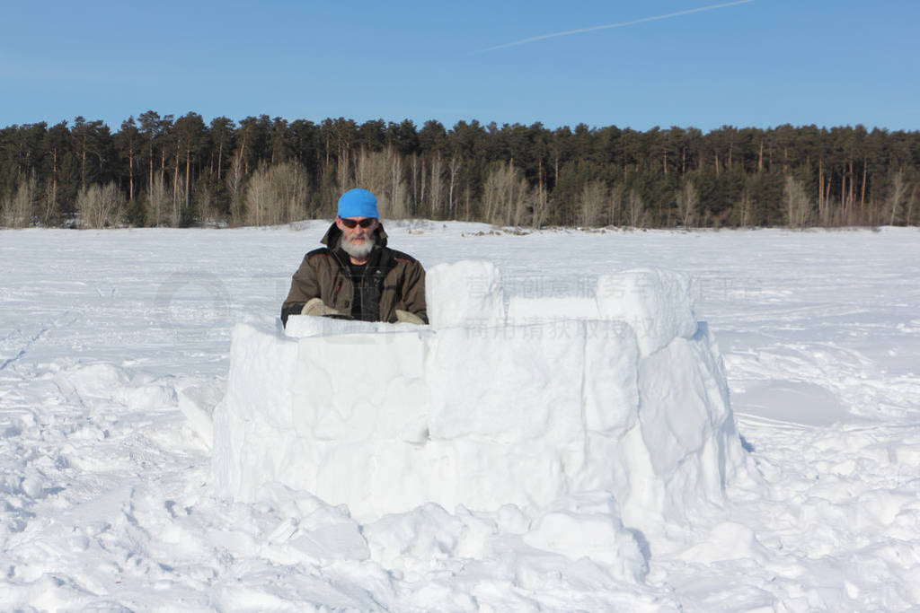 Man in a blue hat building an igloo from snow snow blocks