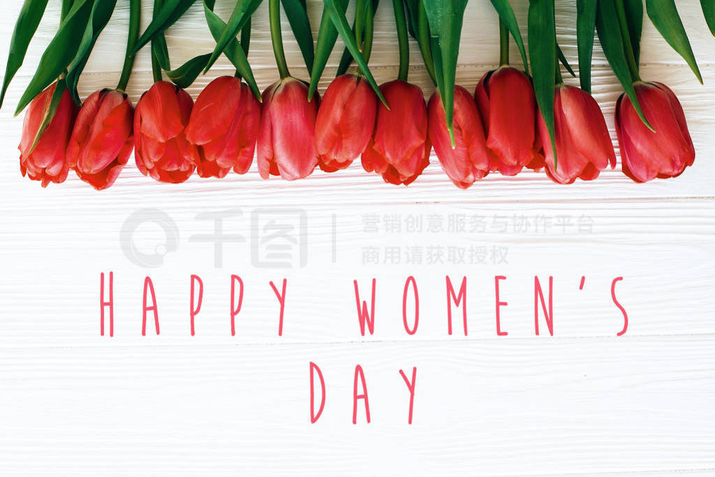 Happy Women's Day text and beautiful red tulips on white wooden