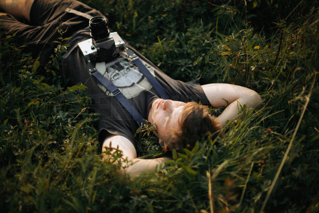 Stylish hipster man with film photo camera lying in green grass