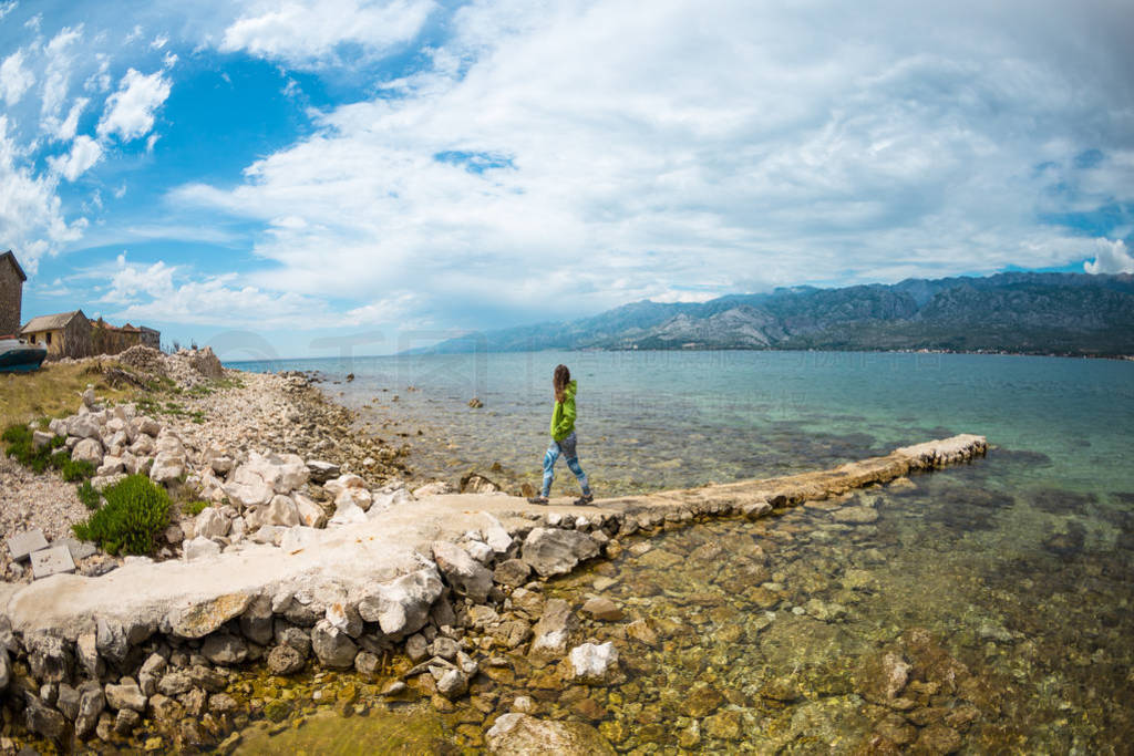 A woman walks along a stone pier.