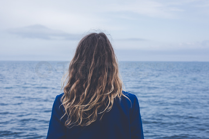 43年轻金发卷曲女孩在看着朦胧的透过厚厚的雾平静的大海和蓝天的背影
