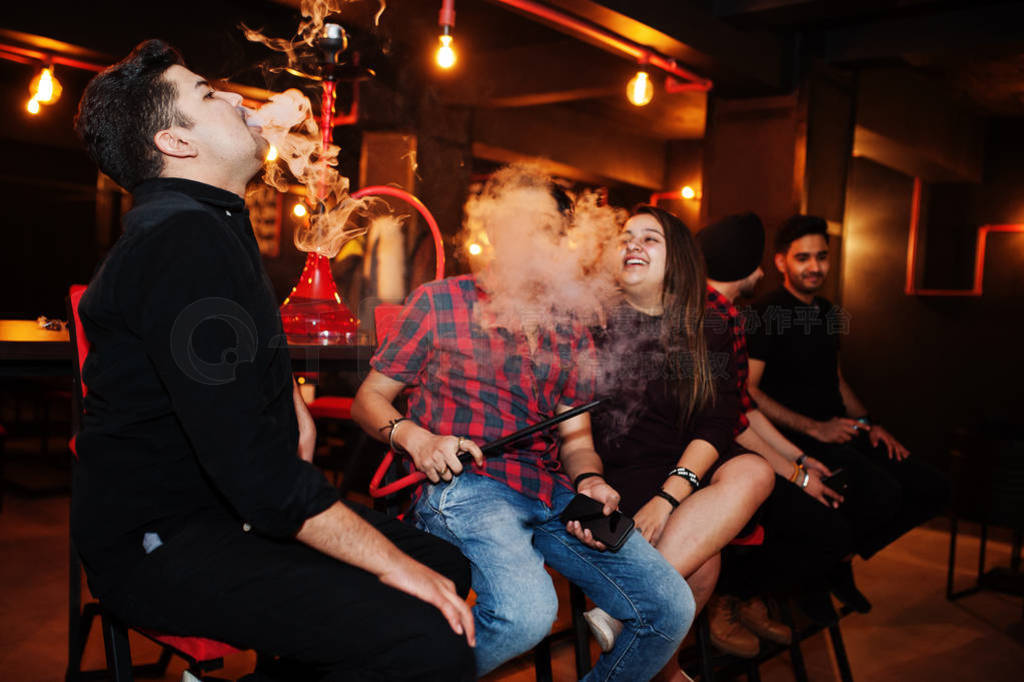 Group of indian friends sitting at lounge bar, smoke hookah and