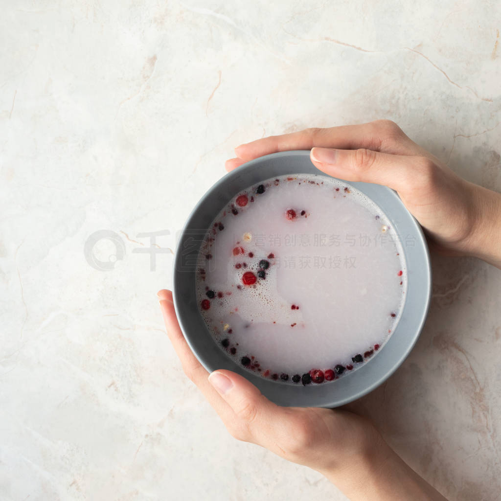 Hand holding gray bowl with oat, berry and milk at breakfast on