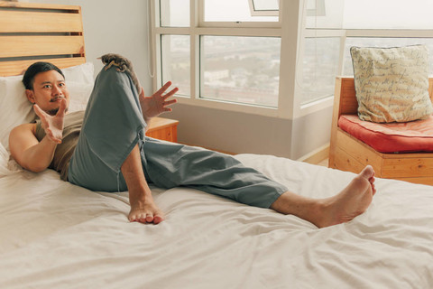 一个亚洲男人躺在床上，在温暖的夏春星期天在他的公寓里放松。