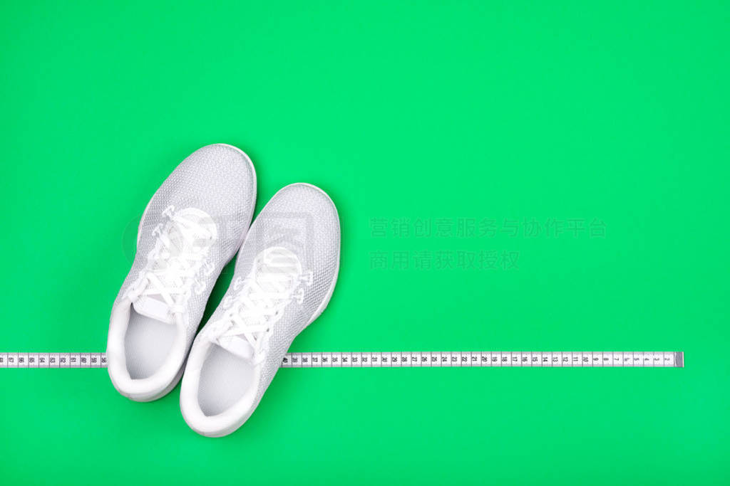 White sport shoes (sneakers) with measuring tape on bright green