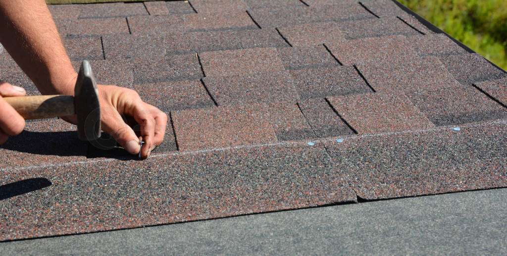 Roofer hands installing asphalt shingles on house construction r