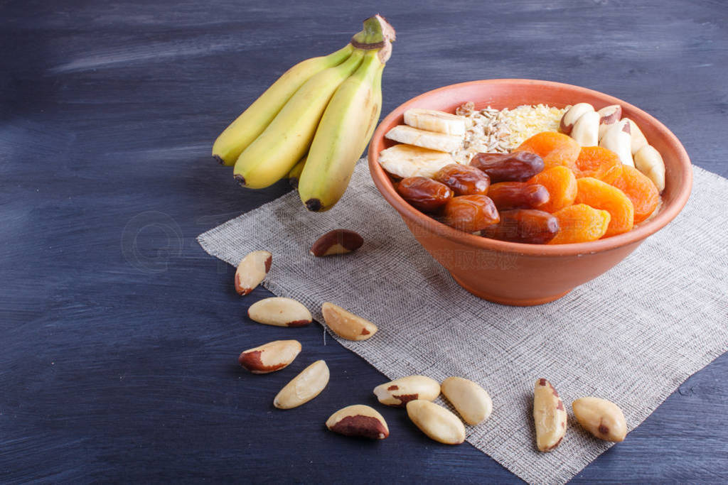 A plate with muesli, banana, dried apricots, dates, Brazil nuts