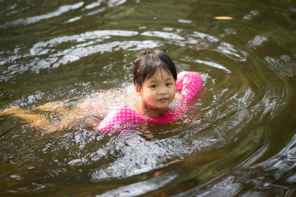 little asian girl wearing inflatable sleeves swimming in nature