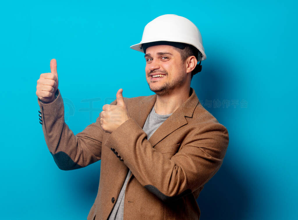 Young engineer in helmet and jacket on blue background