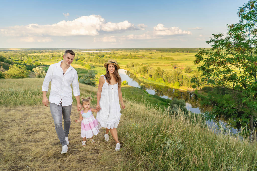 young mom and dad lead their daughter by the hand while walking