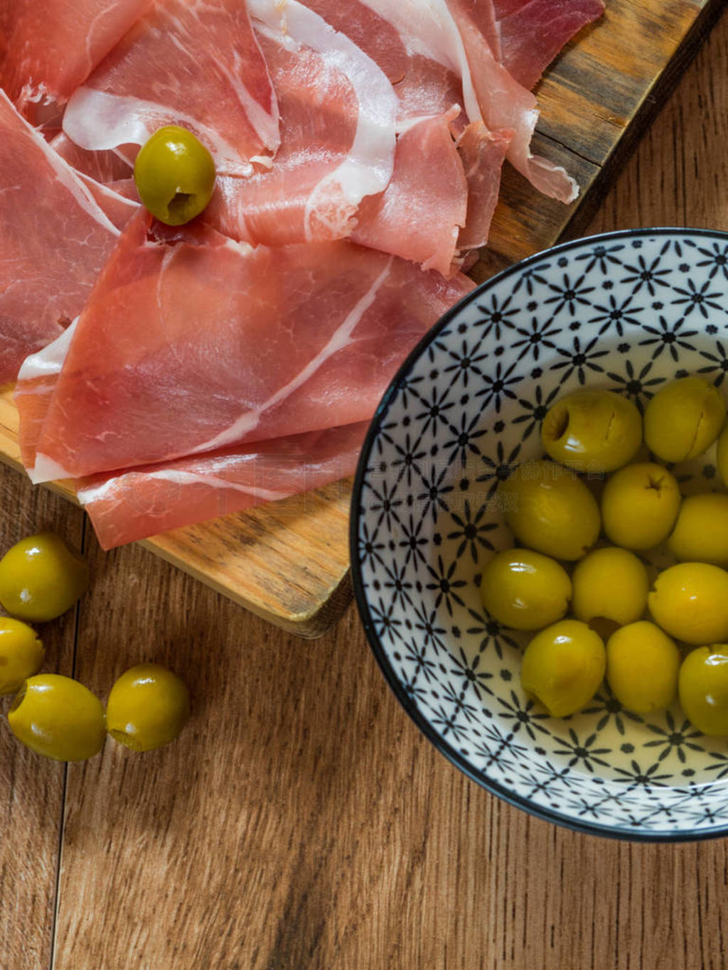 Serrano ham with olives on wood background