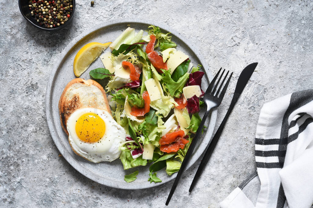 Fried eggs with toast, green salad with salmon