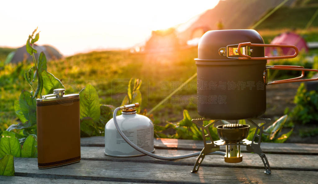 Cooking pot on camping gas stove and hip flask