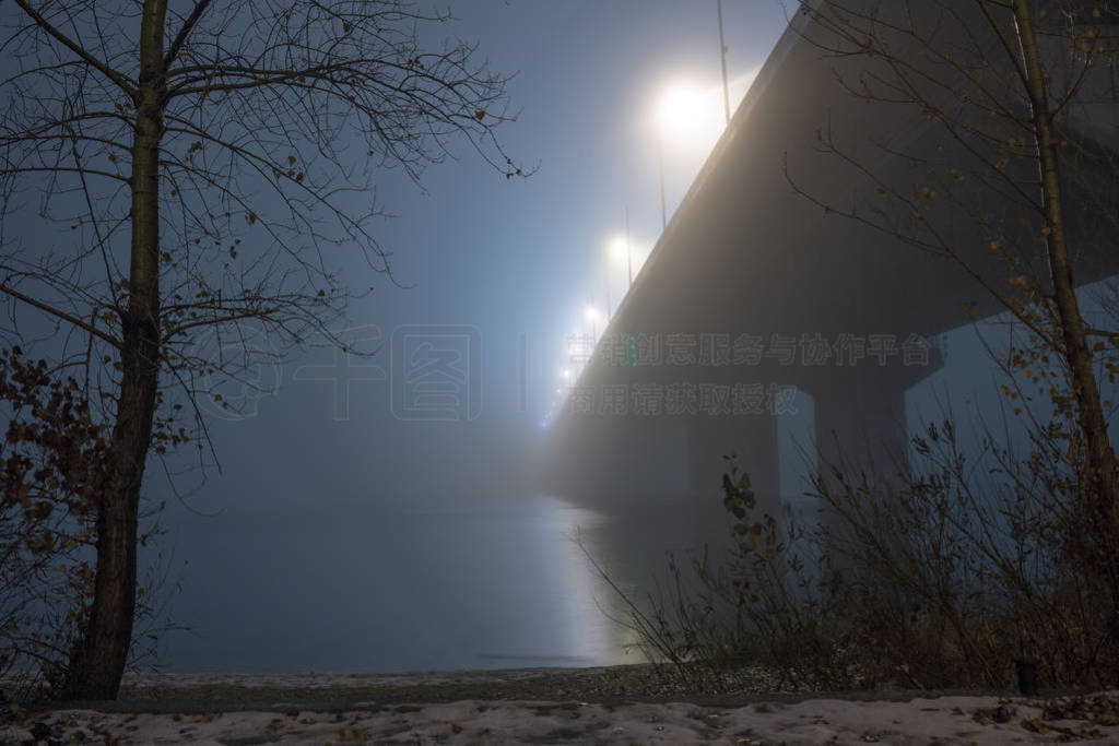 A mysterious evening fog above the river in big city. Bridge in