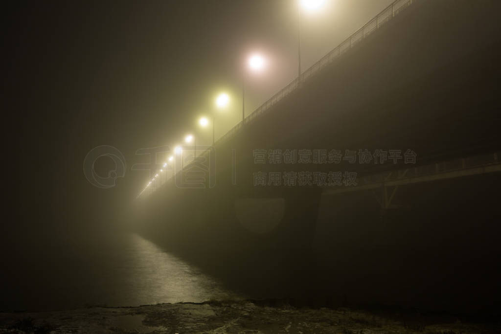 A mysterious evening fog above the river in big city. Bridge in