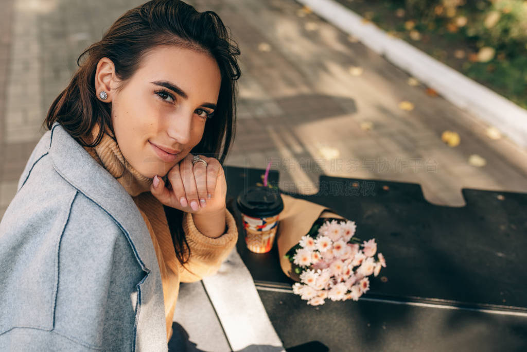 Smiling attractive young woman sitting on the bench and drinking