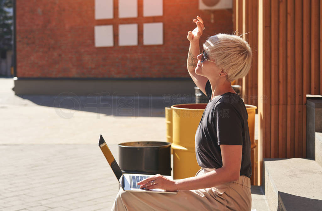 Woman with blonde hair working on laptop sitting outside at stai